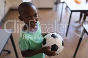 Smiling schoolboy holding football in classroom