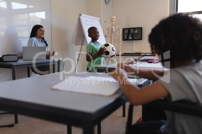 Smiling schoolboy holding football in classroom