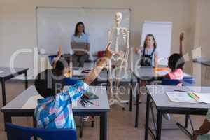 Schoolkids raising hands at desk in classroom