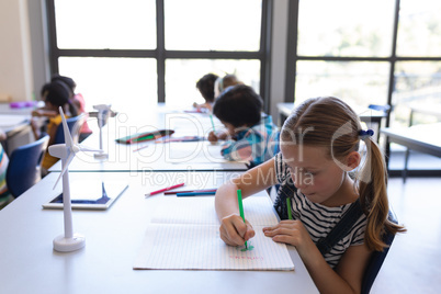 Schoolgirl drawing on book at desk in classroom