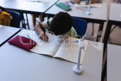 Schoolboy writing on notebook at desk in classroom