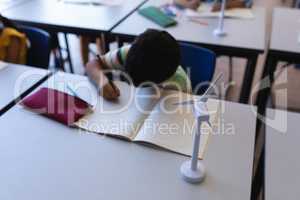 Schoolboy writing on notebook at desk in classroom
