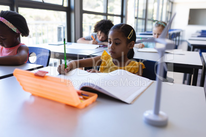 Schoolgirl writing on notebook at desk in classroom