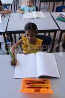 Schoolgirl writing on notebook at desk in classroom