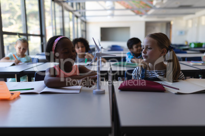 Schoolkids studying on windmill model at desk in classroom