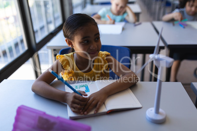 Smiling schoolgirl looking away at desk in classroom