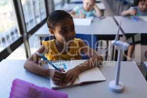 Smiling schoolgirl looking away at desk in classroom