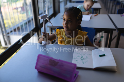 Schoolgirl holding and looking at windmill model at desk in classroom