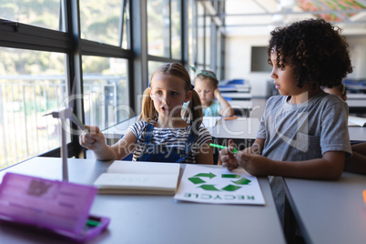 schoolboy discussing over windmill model at desk in classroom