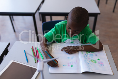 Schoolboy drawing on book at desk in classroom
