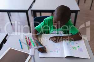 Schoolboy drawing on book at desk in classroom