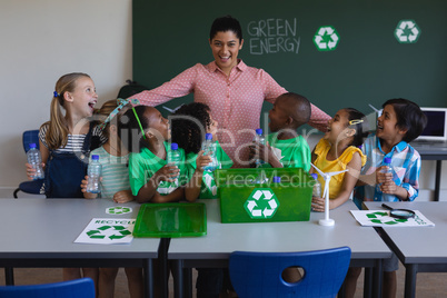 Happy schoolkids looking at teacher on desk in classroom