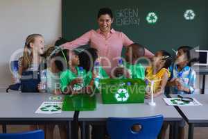 Happy schoolkids looking at teacher on desk in classroom