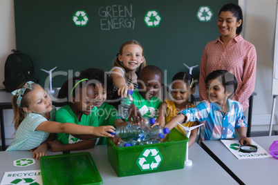 Schoolkids putting bottles in recycle container at desk in classroom