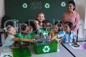 Schoolkids putting bottles in recycle container at desk in classroom
