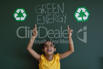 Smiling schoolgirl with arms up standing against green energy board in classroom