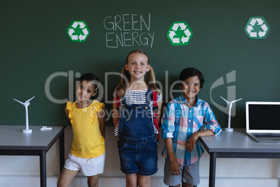 Smiling schoolkids standing against green energy board in classroom