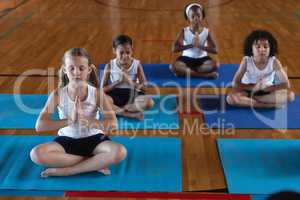 Schoolkids doing yoga and meditating on a yoga mat in school
