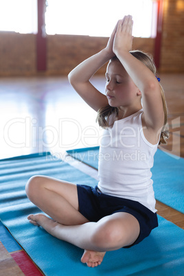 Schoolgirl doing yoga and meditating on a yoga mat in school