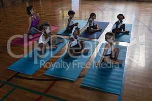 Female yoga teacher and schoolkids doing yoga and meditating on a yoga mat in school
