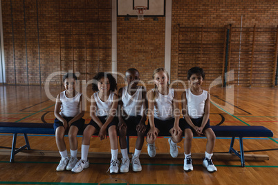 Schoolkids looking at camera while sitting on bench at basketball court