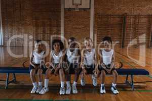 Schoolkids looking at camera while sitting on bench at basketball court