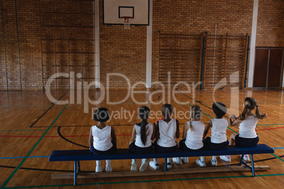 Schoolkids sitting on bench at basketball court