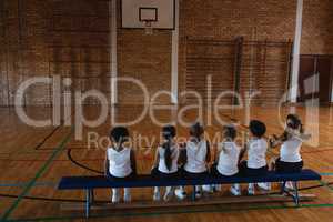 Schoolkids sitting on bench at basketball court