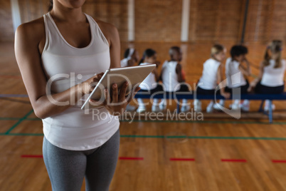 Mid section female basketball coach using digital tablet at basketball court