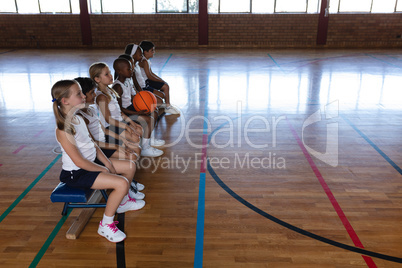 Schoolkids sitting on bench at basketball court