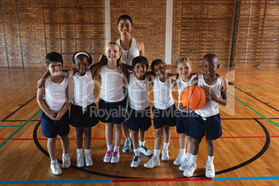 Happy schoolkids and female coach looking at camera at basketball court