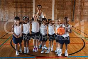 Happy schoolkids and female coach looking at camera at basketball court