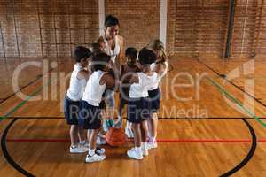 Schoolkids and female coach forming hand stack at basketball court