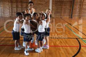 Schoolkids and female coach forming hand stack and looking at camera