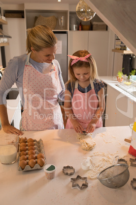 Daughter using cookie cutter while mother looking at her in kitchen