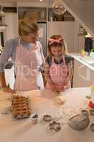 Daughter using cookie cutter while mother looking at her in kitchen