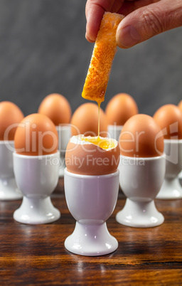 Hand Dipping Toast Soldier Into Boiled Eggs in Egg Cups on a Tab