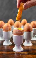 Hand Dipping Toast Soldier Into Boiled Eggs in Egg Cups on a Tab