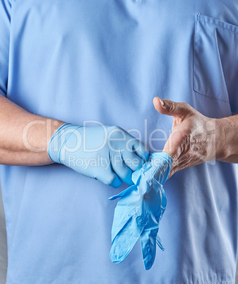 doctor in a blue uniform puts on sterile latex gloves