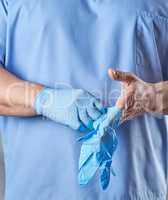 doctor in a blue uniform puts on sterile latex gloves