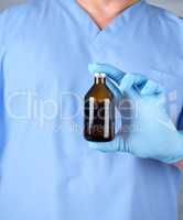 doctor in blue uniform and latex gloves holding a brown glass bo