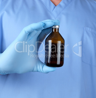 doctor in blue uniform and latex gloves holding a brown glass bo