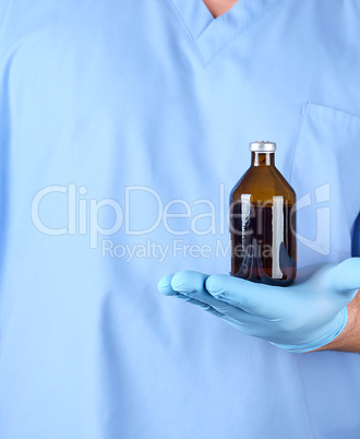 doctor in blue uniform and latex gloves holding a brown glass bo