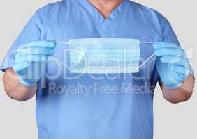 doctor in blue uniform and latex gloves holding a medical mask