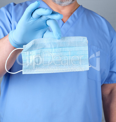 doctor in blue uniform and latex gloves holds a medical mask