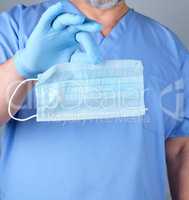 doctor in blue uniform and latex gloves holds a medical mask