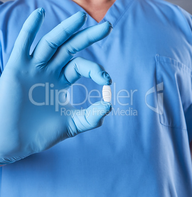 doctor in blue latex gloves holding a white pill