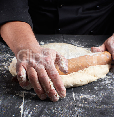 chef in a black tunic rolls a dough for a round pizza