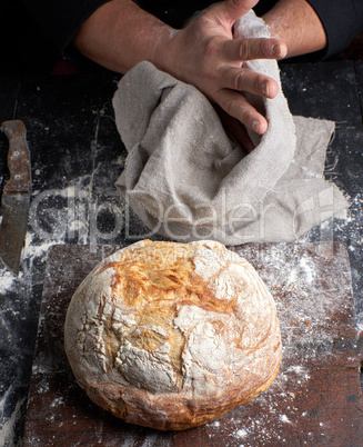 baked round bread on a board, behind the cook in black clothes