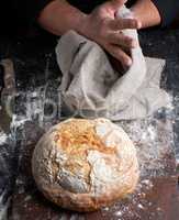 baked round bread on a board, behind the cook in black clothes